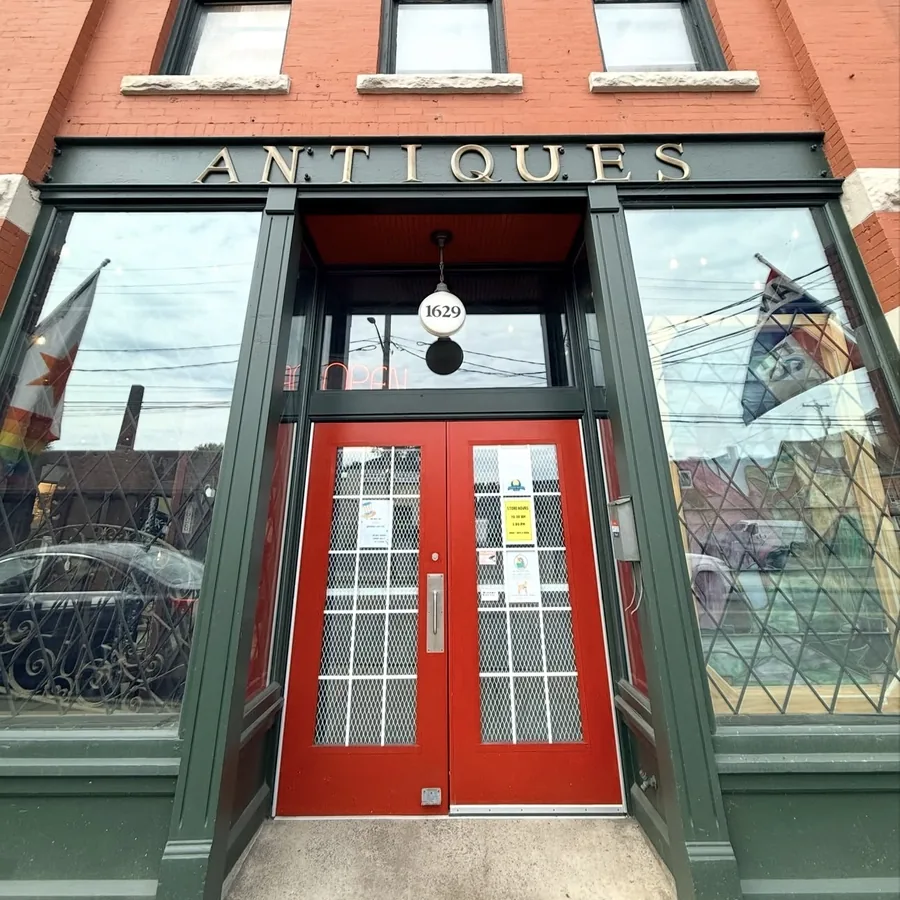 The Syracuse Antiques Exchange storefront on North Salina Street, with red double doors under brass ANTIQUES signage and a lit 1629 globe lamp overhead
